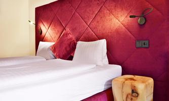 A cozy bedroom with a red padded headboard and two blankets. Next to the bed stands a wooden nightstand.