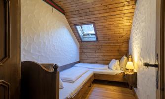 A cozy bedroom with wood paneling and a window. There are two beds and a bedside lamp available.