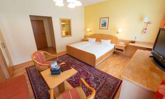 A cozy hotel room with a double bed and a small table. The walls are painted in a warm yellow tone and there is a comfortable seating area.
