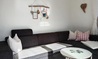 A cozy living room with a dark gray couch and cushions in light colors. Decorative pictures and accessories hang on the wall.