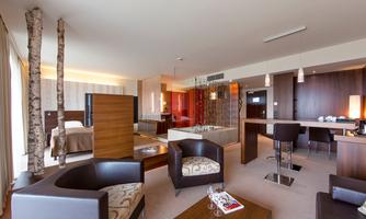 A modern hotel room with stylish furnishings. There are comfortable sofas, a table, and an open kitchen.