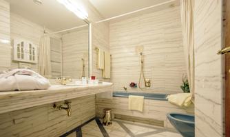 An elegant bathroom with marbled walls and a bathtub. Towels and toiletries are arranged on the vanity.