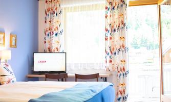 A cozy bedroom with a large bed and a desk. The room has blue walls and bright curtains that let in plenty of daylight.