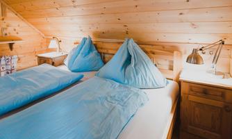 A cozy bedroom with wooden walls. There is a double bed with blue bedding and two nightstands.