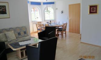 A bright living room with modern furniture. There is a dining table and large windows that let in a lot of light.
