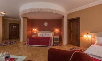 A cozy room with two beds, a red bedspread, and an elegant carpet. The walls are painted in warm colors, and two nightlights create a pleasant atmosphere.