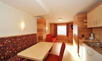 A modern kitchenette with a dining table and a cozy seating area. The room has light walls and large windows for plenty of light.