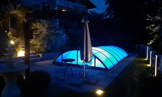 A beautiful garden area at night with a illuminated swimming pool. The blue lights create a relaxing atmosphere.