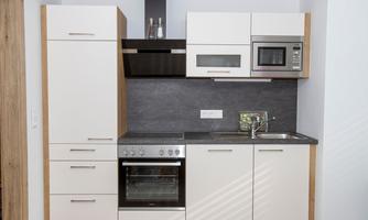 A modern kitchen with white and wood-colored cabinets. It features a stove, a dishwasher, and a microwave.