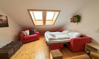 A cozy room with a skylight and wooden floor. There is a large bed, two red sofas, and a small dresser.