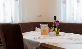 A cozy table with a table runner, a bottle of wine, and a decorative flower. The room is bright and inviting with large windows.