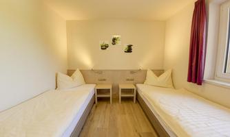 A simple room with two single beds and modern accents. The walls are bright and there is a window with natural light.