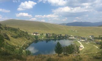 A peaceful landscape with a clear lake and gentle hills in the background. The sky is partly cloudy and the surroundings are green and inviting.