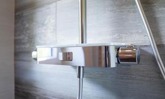 A modern shower faucet made of shiny metal. The faucet is mounted on a light-colored wall and looks elegant and functional.