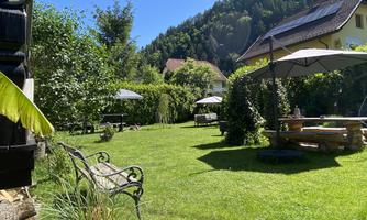 A beautiful garden with green grass and several seating areas. In the background, trees and the mountains are visible under a clear blue sky.