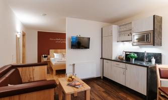 A modern living room with a kitchenette and a television. The decor is bright and cheerful, ideal for a comfortable stay.