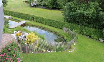 A beautiful garden with a pond and colorful flowers.  
Surrounded by lush greenery and a wooden fence.