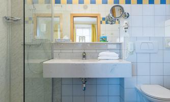 A modern bathroom with a glass shower and a white sink. The floor is tiled in blue and the walls are light with colorful accents.