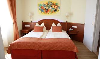 A cozy hotel room with two single beds and a warm, orange blanket. A colorful piece of artwork hangs on the wall.