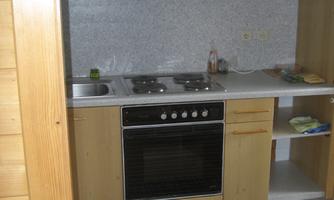 A modern kitchen with wooden shelves and a gray countertop. The equipment includes a stove, a refrigerator, and a sink.