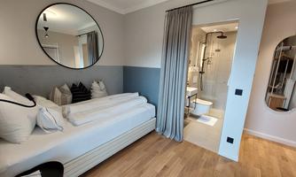 A modern room with two beds and a large mirror. The bathroom is separated by a curtain and elegantly designed.