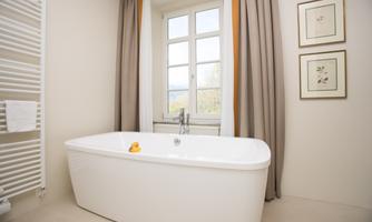 A modern bathroom with an elegant bathtub and large windows. Soft colors and decorative pictures create a relaxing atmosphere.