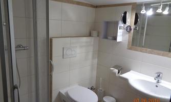 A modern bathroom with a shower and sink. The walls are brightly tiled and there is a toilet as well as a mirror.