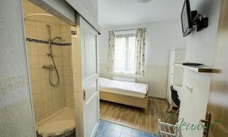 A simple and modern room with a single bed and a bathroom with a shower. The room has a window with curtains and a television on the wall.