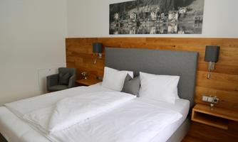 A modern bedroom with a large double bed and bright wood decor. A picture of a tranquil landscape hangs on the wall.