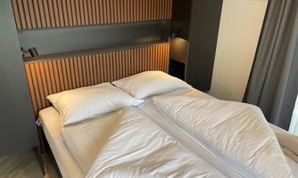 A modern bedroom with a large bed and bright pillows. The walls are designed with wooden slats and the room has soft lighting.