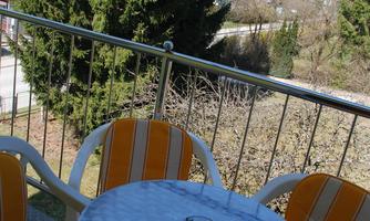 A balcony with two orange chairs and a small round table. In the background, there are trees and a blue sky.