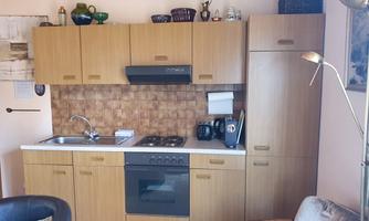 A modern kitchen unit with wooden cabinets, stove, and sink. Kitchen appliances and decorative items are placed on the countertop.