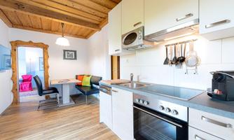 Modern kitchen with wooden ceiling and dining area. It is bright and well-equipped with appliances and utensils.