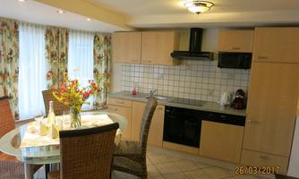 A modern kitchen with a dining area. The table is decorated with a vase of flowers, and there are bright curtains that create a cozy atmosphere.