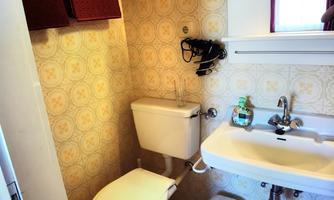 A small bathroom with a toilet, a sink, and a mirror. The walls are decorated with a beige-yellow wallpaper.