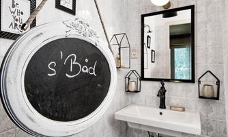 A modern bathroom with a sink and a mirror. On the wall hangs a decorative chalkboard with the inscription "s'Bad".