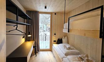 A modern room with light wooden walls and two single beds.  
Large windows provide plenty of daylight and a view outside.