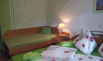 A cozy room with green walls and wooden furniture. There is a bed, a seating area, and decorative cushions.