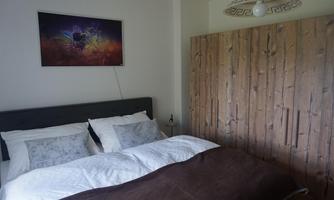 A cozy bedroom with a large bed and a wooden dresser. A modern artwork hangs on the wall.