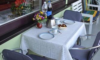 A beautifully set table on a balcony with two chairs. There are water bottles, a coffee pot, and small treats on the table.