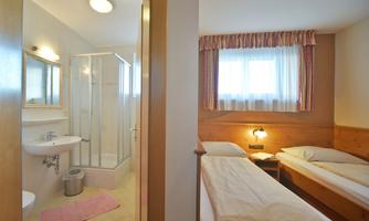 A simple room with two single beds and a bathroom. The room has a window with natural light and a bright, friendly atmosphere.