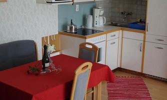 A cozy kitchen with a red table and chairs. On the table are flowers and a bottle of champagne.