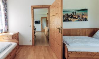 A bright room with two wooden beds and an open door area. A picture of a peaceful coastal landscape hangs on the wall.