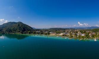 A picturesque landscape with a clear lake and surrounding mountains. The sky is blue with a few clouds.