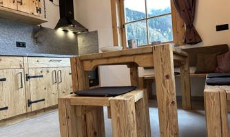 A cozy kitchen with wooden furniture and a dining table. Through the window, you can see the mountains and nature outside.