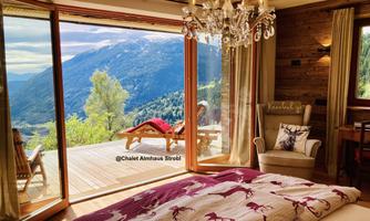 A cozy bedroom with a view of a picturesque mountain landscape. Large windows provide access to the terrace, which is equipped with deck chairs.