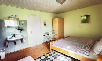 A simple room with two beds, a table and chairs. The walls are light green, and there is a small sink as well as a wardrobe.
