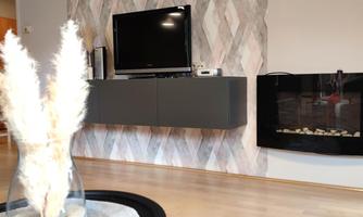 A modern living room with a TV on the wall and an elegant fireplace. A vase with dried flowers sits on a round table in front of a soft rug.