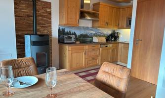 A cozy kitchen with wooden cabinets and modern amenities. The dining area with a table and glasses creates an inviting atmosphere.