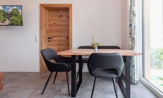 A modern dining room with a wooden table and black chairs. A large window front lets in a lot of light.